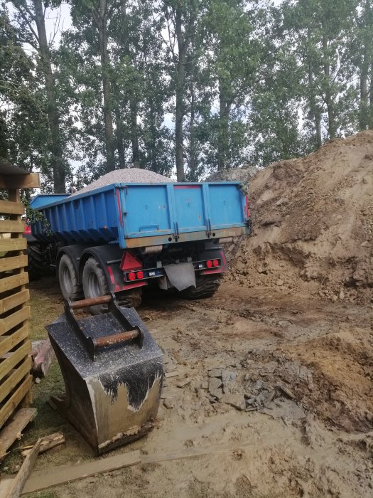 Lastbil tippar grus för återfyllning vid sättning av brunn i byggprojekt.