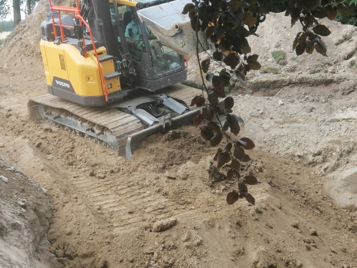 En grävmaskin av märket Volvo gräver i en sandhög vid ett byggprojekt.