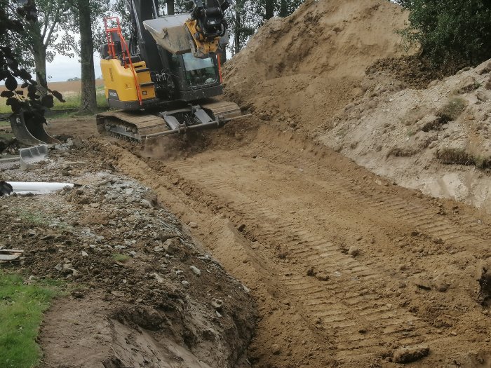 Grävmaskin i arbete vid grävning av en grävd schakt för fundament eller rörledning i jordbruksmiljö.