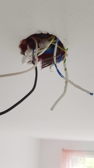 Okopplade elkablar hänger från ett öppet uttag i taket mot en vit bakgrund.