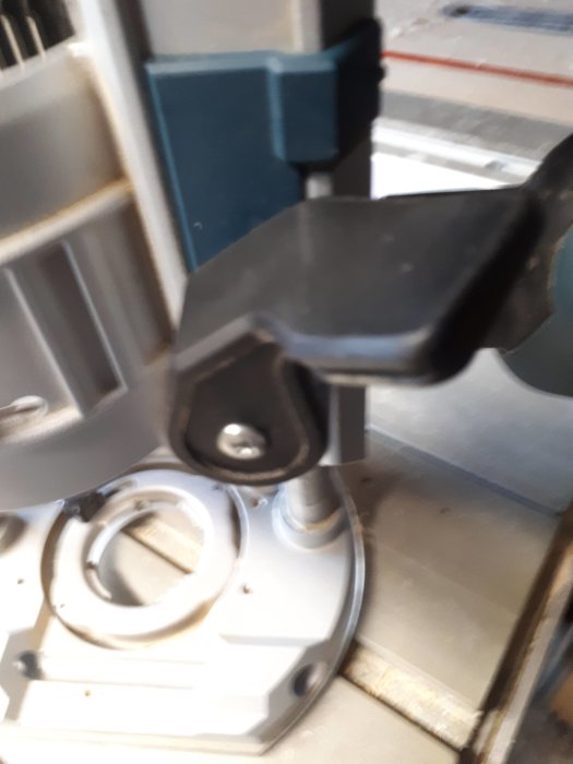 Närbild på en grå maskindel med en svart justerbar knapp och sexkantsskruv i fokus.