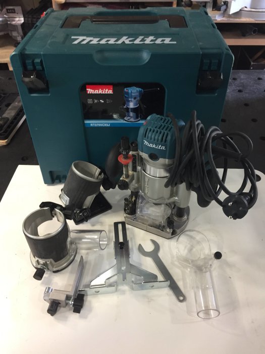 Makita RT0700CX5J fräspaket med olika tillbehör utspridda framför dess blå förvaringslåda.