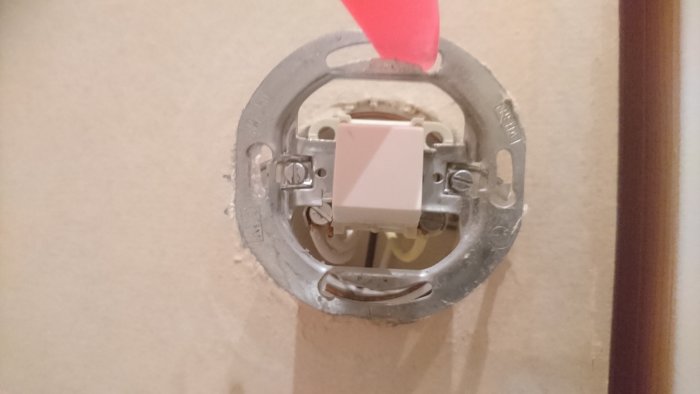 Elektrisk installationsdosa monterad i vägg med öppet borrhål och synliga kablar.