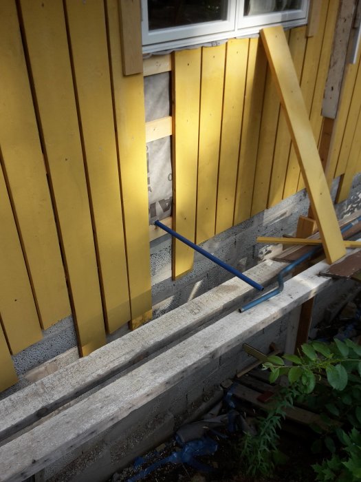 Påbörjat arbete på husfasad med ny panel, verktyg synliga, vid ett fönster.