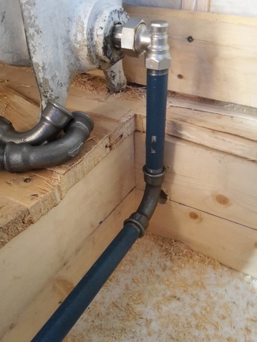 Nyinstallerad vattenrörskoppling med metall- och plastdelar i ett träkonstruerat utrymme.