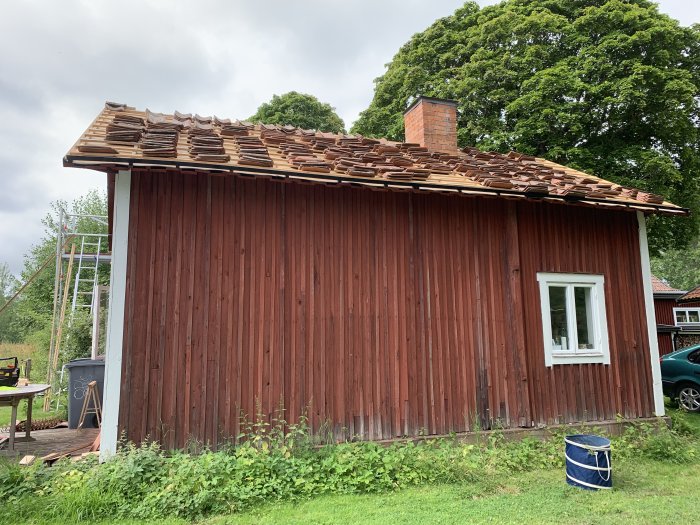 Rött trähus med nytt tegeltak nästan klart, stegar vid sidan, skorsten utan krage.