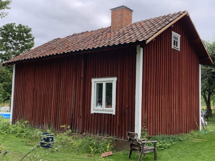 Nyinstallerat tegeltak på en rödmålad stuga med vit skorsten och fönsterkarmar, trädgård i förgrunden.