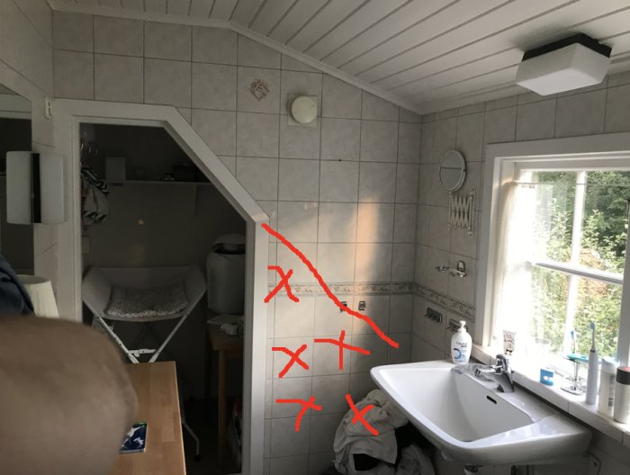 Bathroom with sloped ceiling, sink beneath window, and red markings on tiled wall indicating potential remodel of a wall near a doorway.
