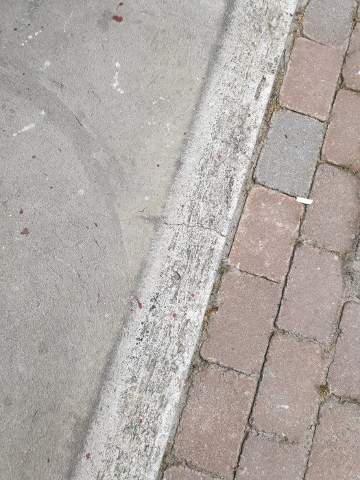 Sliten betongplatta vid garageuppfarten bredvid rödaktiga trottoarstenar.
