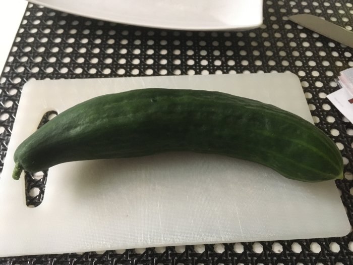 En frisk grön gurka liggande på en vit skärbräda.