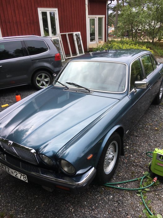 En grön Jaguar XJ6 serie 3 från 1985 parkerad framför en röd byggnad, redo för service.