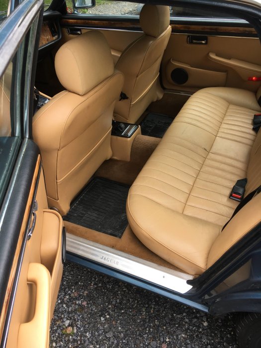 Interiör av Jaguar XJ6 med beige lädersäten och träpaneler, dörrtröskel märkt med 'JAGUAR'.