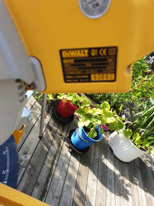 Gult DeWalt verktyg från översiktsvinkel med suddig närbild av märkning, på en terrass med blomkrukor i bakgrunden.