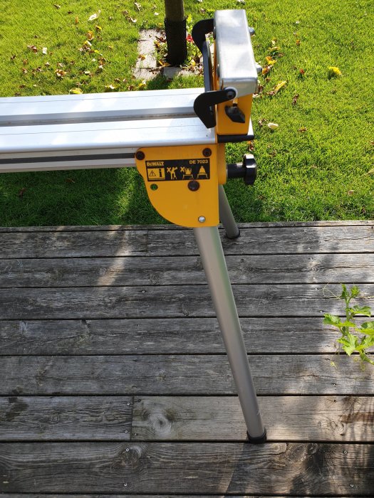 Gult och grått DEWALT arbetsbänksstativ modell DE 7023 på en trätrall utomhus.