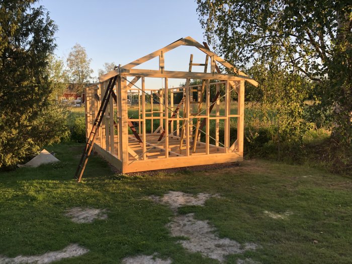 Uppförande av trästomme till byggnad med den första takstolen på plats i solnedgång.
