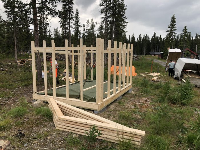 Byggande av ett 12 kvm stort förråd med träpanel, stomme uppe, människor arbetar i bakgrunden.