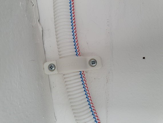 Elektriska kablar i korrflexrör säkrade mot en vit vägg med en kabelklämma.