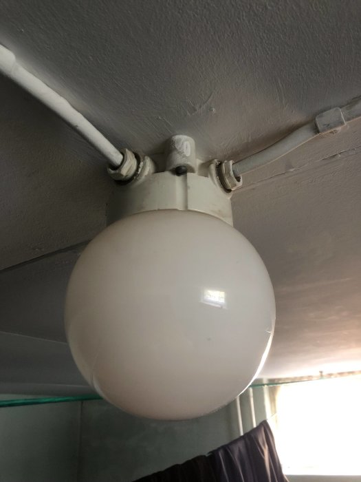 Taklampa med vit glödkupol kopplad till vägg via metallfästen i en källare.