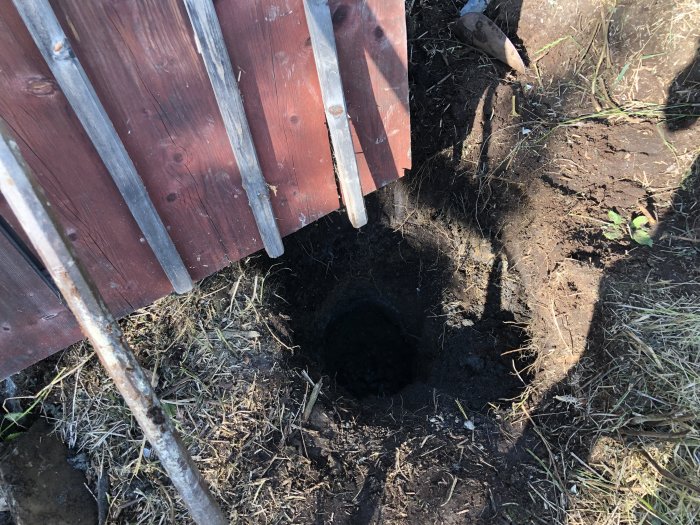Bild av ett nyligen påbörjat grävt hål intill en röd trästaket – problem med grundvattnet nära sjön.