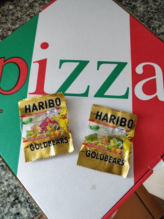 Pizzakartong med texten "izza" synlig och två små påsar HARIBO Goldbears framför.