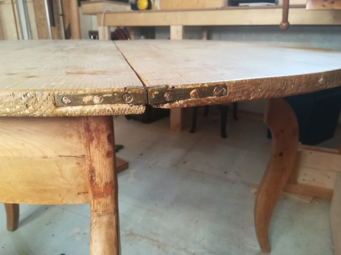 Gångjärn på en ihopfälld träbordskant med synlig avsmalnande tjocklek och skruvar.
