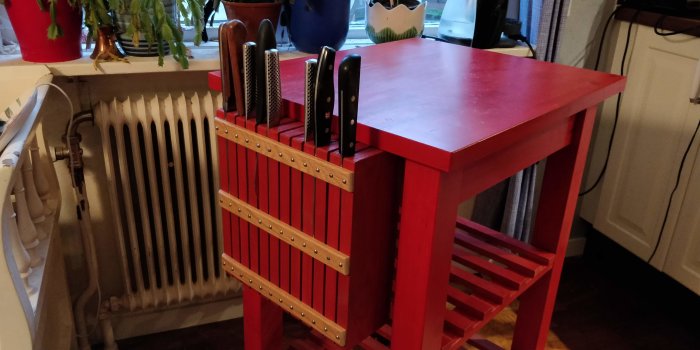 Rödmålat rullbord med skräddarsytt knivblock av fur och ek, med knivar i olika storlekar insatta.