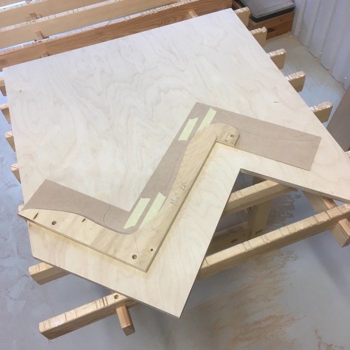 Plywoodskiva med utskurna trädelar till möbel, verktyg och trälim på arbetsbänk.