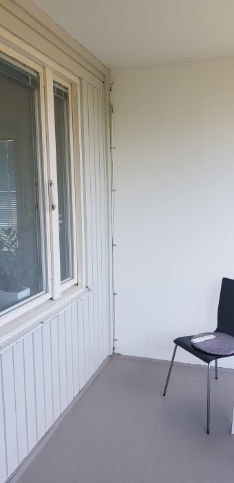Två kablar klamrade längs en vit vägg på en balkong, intill ett fönster och en stol.