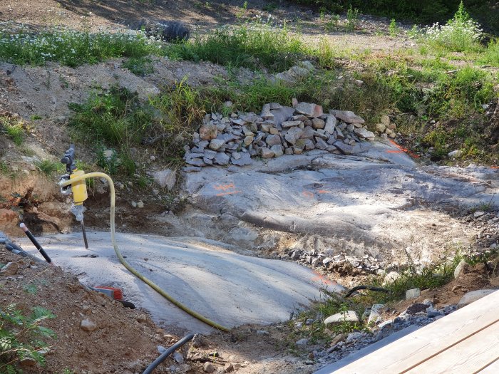 Byggplats med grävd grop och en hög av stenar, markerade linjer på berg och byggutrustning.