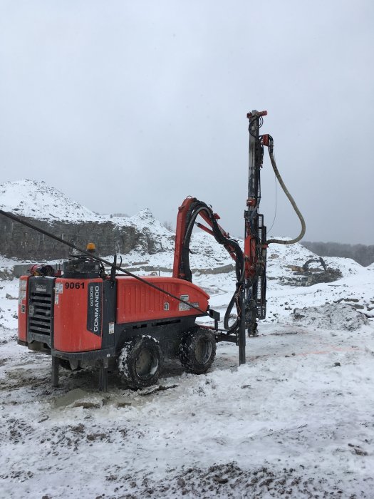 Röd Sandvik Commando 9061 bergborrigg i ett snöigt grustag.