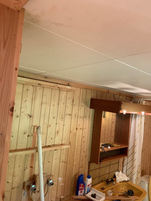 Renoveringsbehov i bastu med lågt innertak, träpanel och gammal plastmatta på golvet.