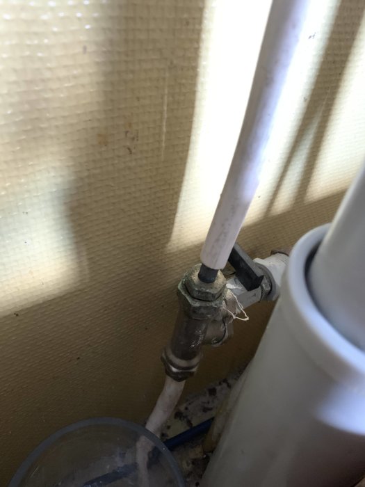 Vattenrör med avstängningsventil täckt av aluminiumfolie, placerad nära en vägg och golv.