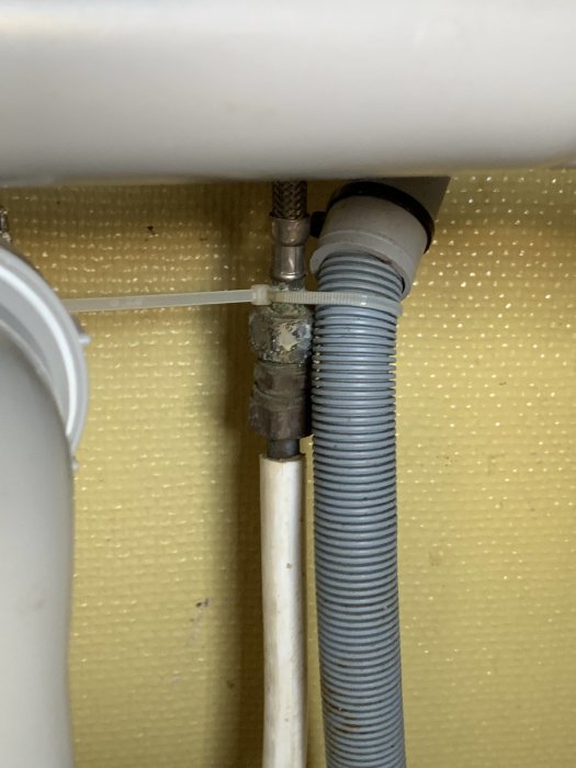 Rörsystem under diskbänk med kopplingar och aluminiumfolie runt en läckande del.