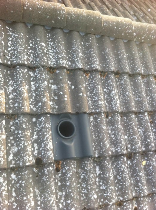 Tegeltak med en öppen ventilationsrör och lätt snötäcke.