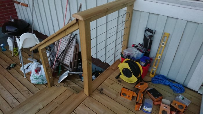 Träräcke på veranda med nyinstallerat vajerräcke och diverse verktyg och byggmaterial i förgrunden.