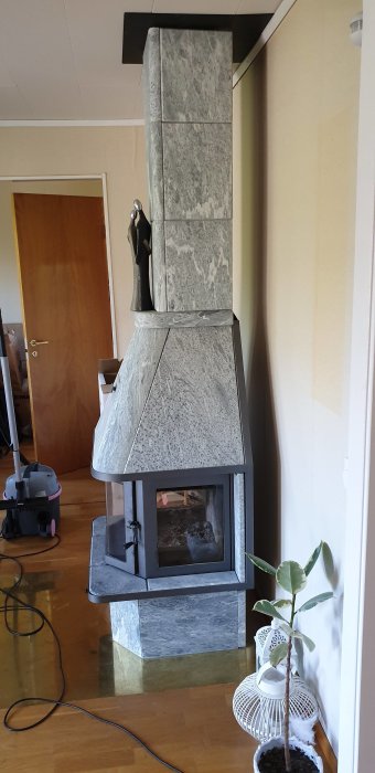 En stående kamin klädd i sten med synlig eldstad i ett vardagsrum, med en fråga om flyttning vid renovering.