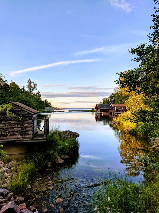 Idyllisk utsikt över en lugn sjö vid Furuvik med en stuga och grönska omkring i skymningen.