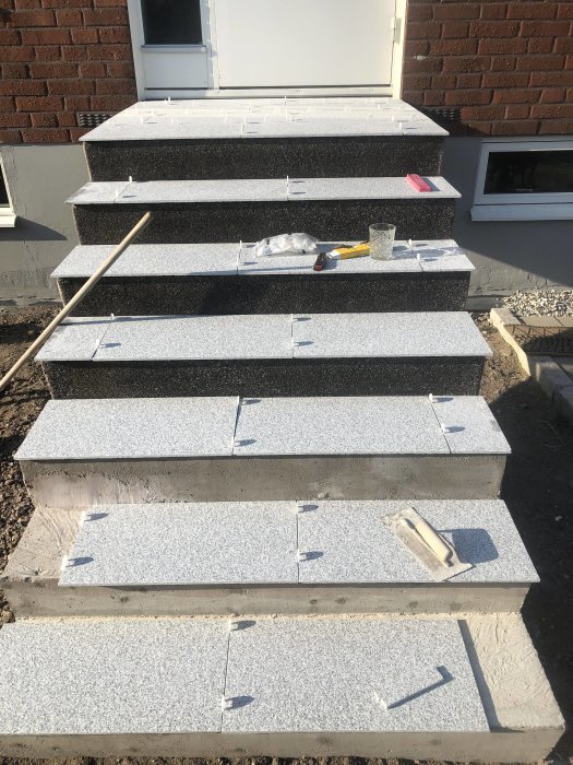 Utetrappa under renovering, delvis klädd med granitsten, byggverktyg synliga.