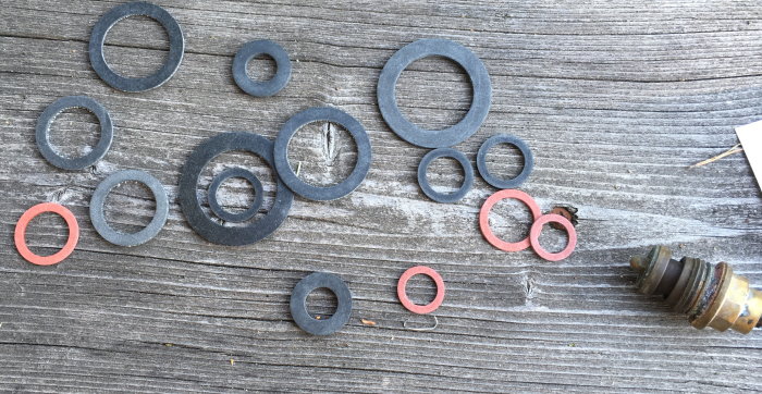 Olika storlekar av gummipackningar utspridda på träyta bredvid en demonterad ventilinsats.