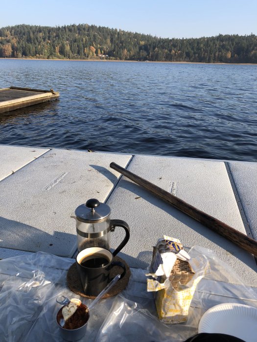 Fikapaus på bryggan med kaffekanna, macka och sjöutsikt i soligt väder.