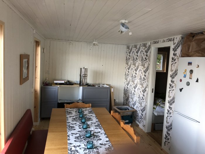 Interiör av ett kök under renovering med vita väggar, tapet, och en ännu ej komplett köksinredning.