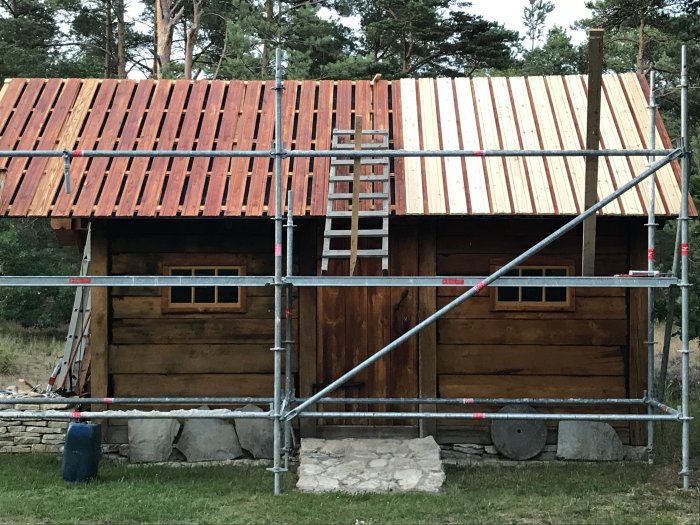 En stuga under renovering med halvklart tak och byggnadsställningar runtomkring.