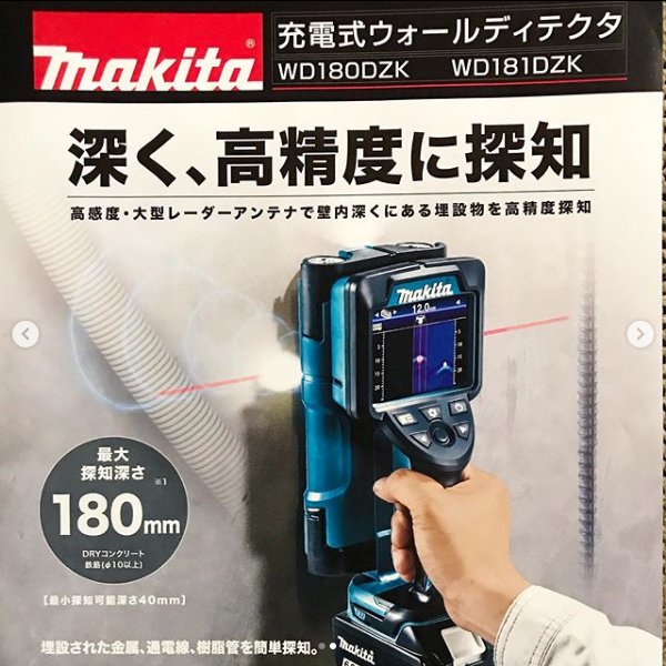 Hand håller en Makita väggsökare framför en reklamaffisch med japanska tecken.