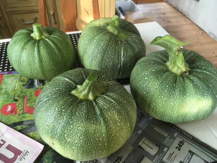 Fyra gröna squashar ligger på en tidning ovanpå ett köksbord.
