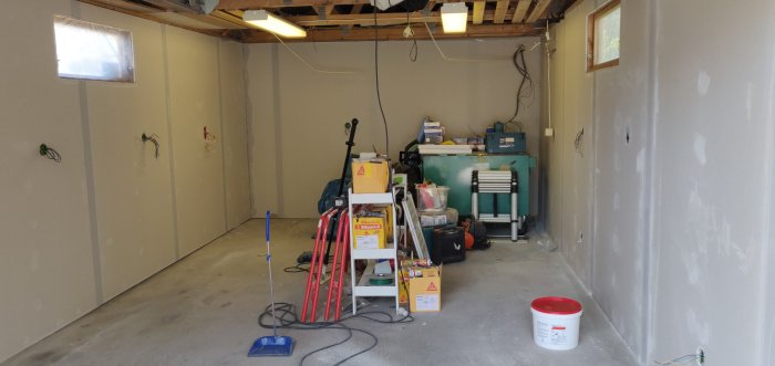 Renoveringsarbete i ett garage med isolerade gipsväggar och utsatta elektriska uttag, samt verktyg och byggmaterial utspridda på golvet.