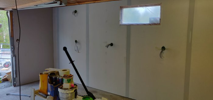 Garage under renovering med ny isolering och gipsväggar, synliga elinstallationer och byggmaterial på golvet.