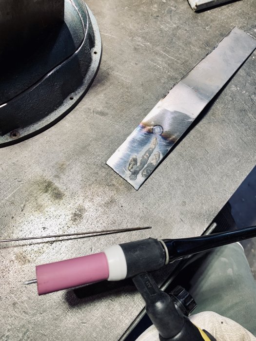 Tiglödning av ett metallstycke på en arbetsbänk bredvid slipade ventilationsdelar, indikerar reparation av verktygsmaskin.