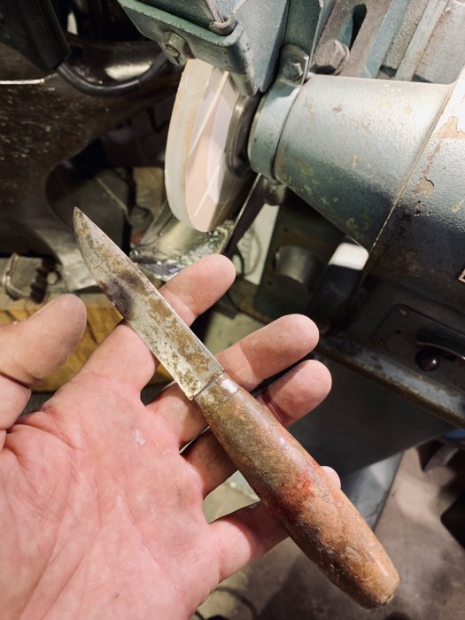 Hand håller en sliten morakniv framför en slipmaskin för slipning och återställning av skärpan.