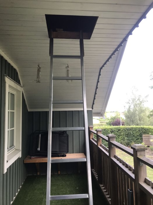 En aluminiumstege står på en veranda framför en öppen lucka i taket som leder till vinden.