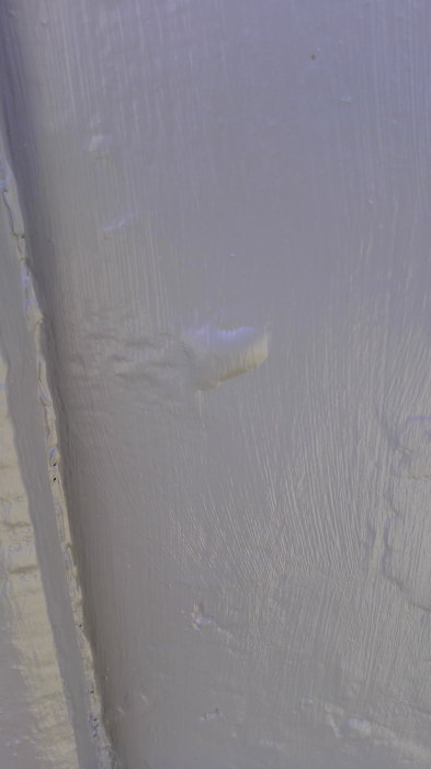 Skadad målningsyta på husvägg med blåsor och synlig grundfärg vid skarv.